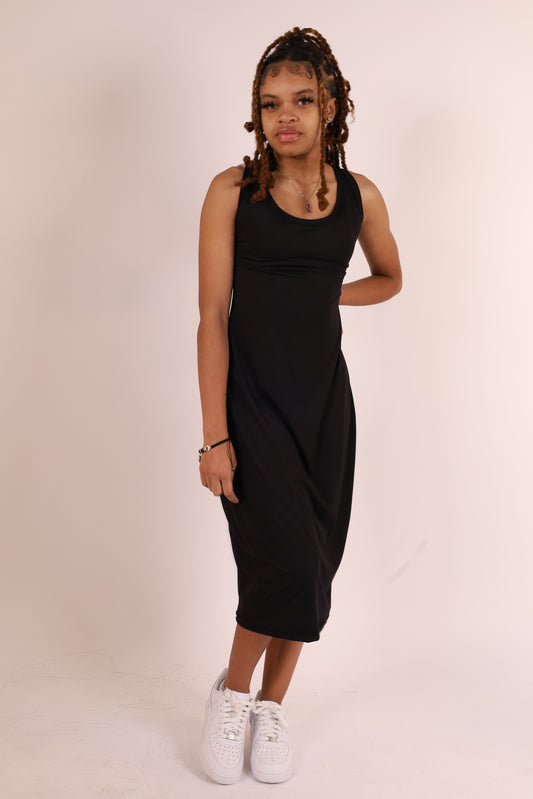 A person standing against a white background, wearing a black sleeveless maxi dress with a V-neckline and a midi length.